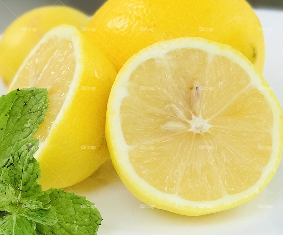 One lemon cut into two slices, and background covered with lemon’s and there also a mint leaves.