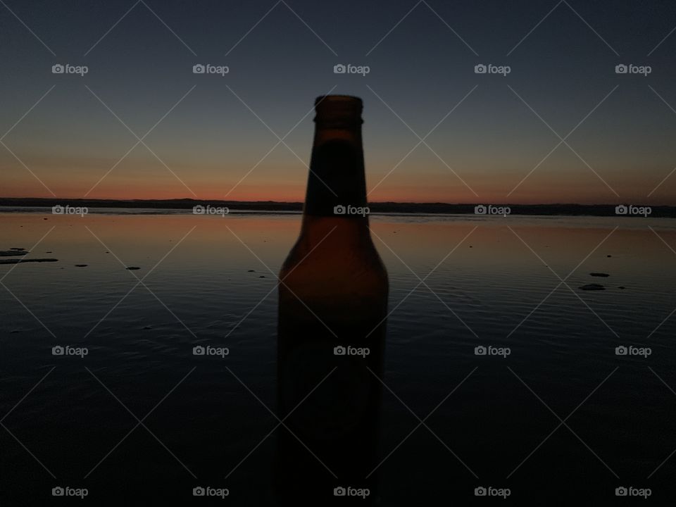 Icy beer silhouetted against the warm amber sunset of the wild west coast beach of New Zealand. 