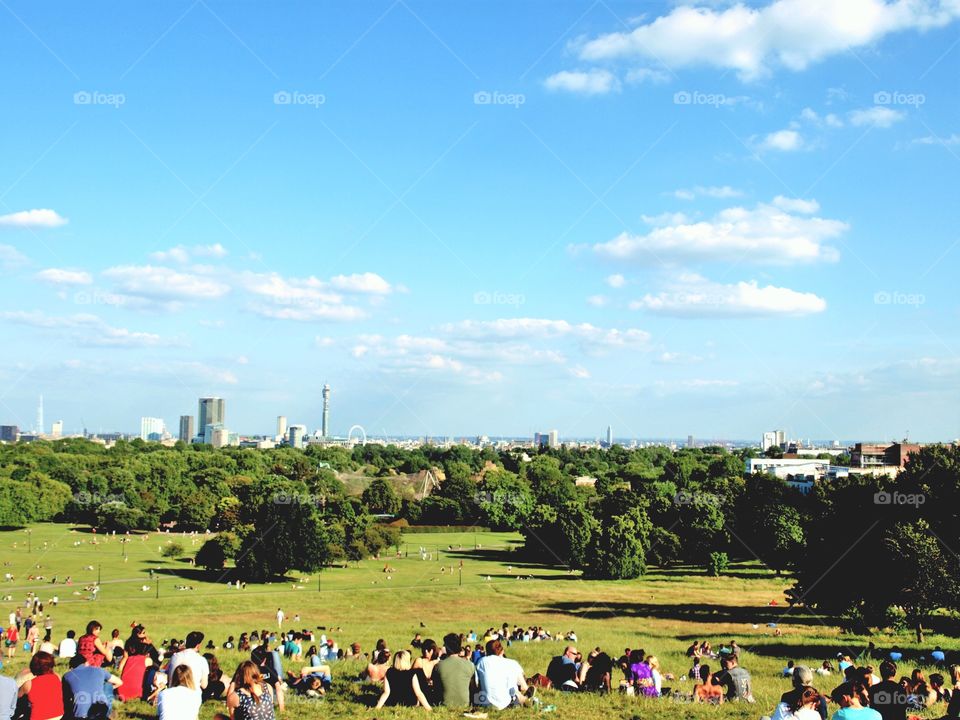 People sat on Primrose Hill, London on a sunny day with an amazing view of the London skyline 