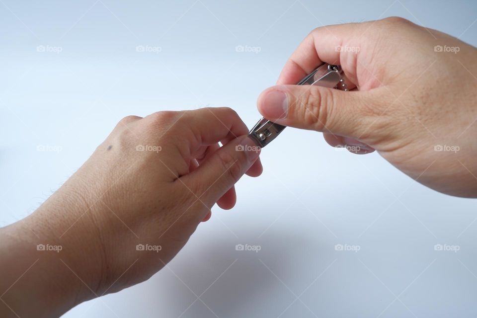 Man cuts his nails with nail clippers on a white background.
