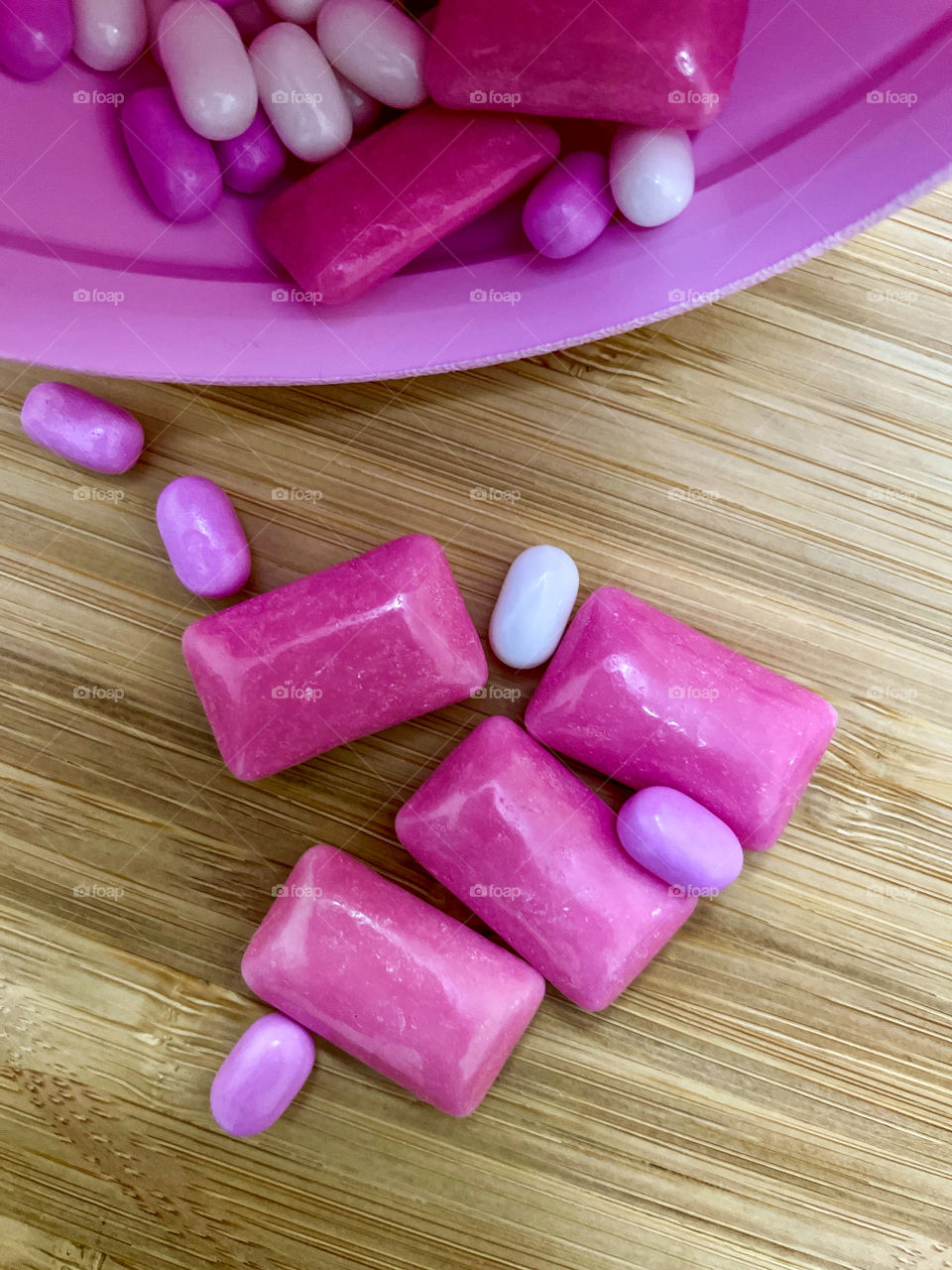 Pink tic tac and bubblegum sweets on a wooden board 