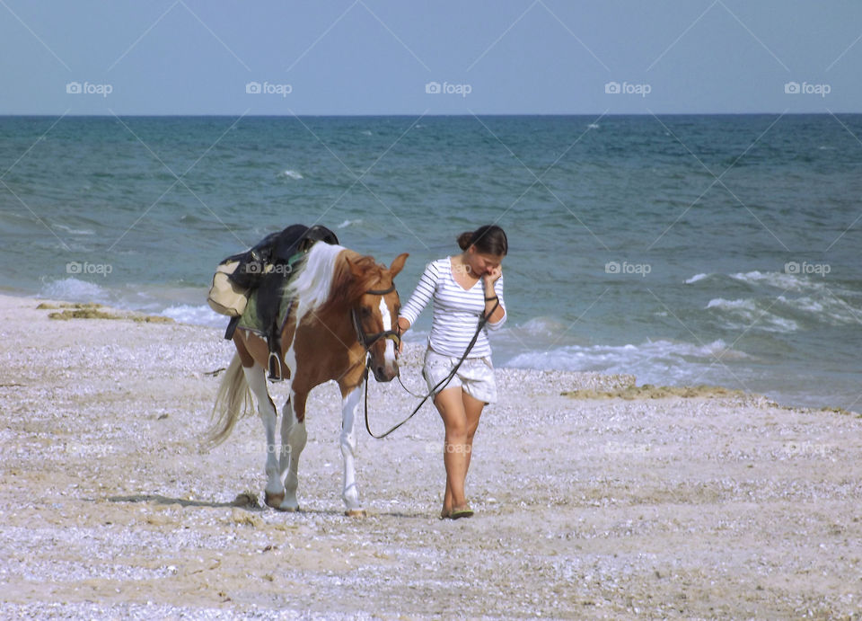 Girl with a horse walking along the seashore