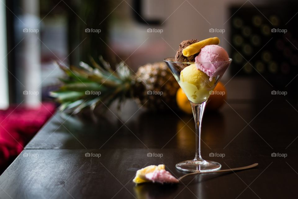 Scoops of ice cream in glass on wooden table decorated with pineapple