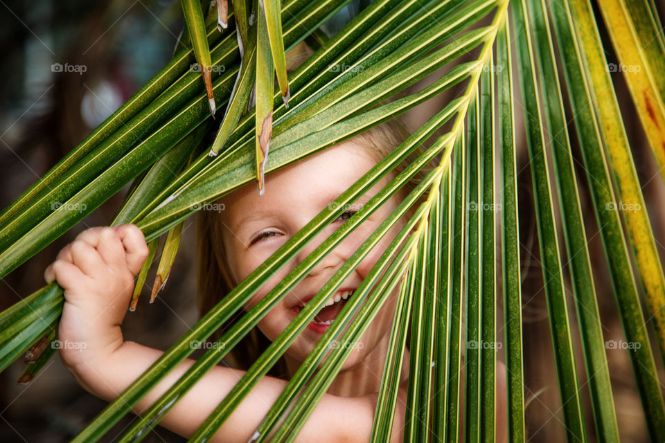 Happy little girl with blonde hair and palm leaf