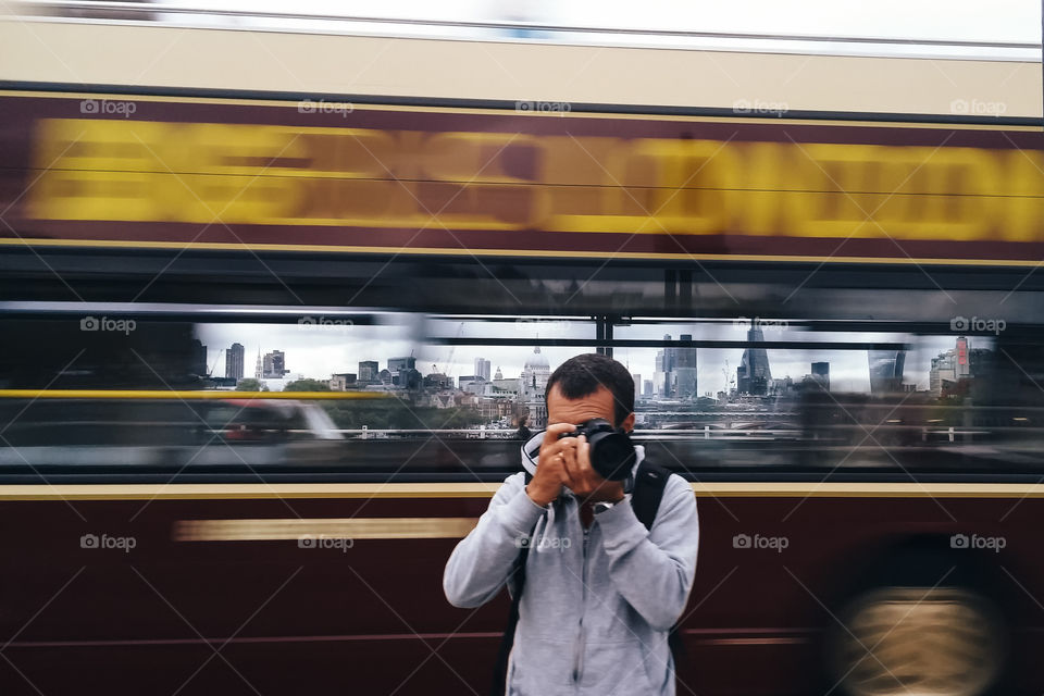 Photographer in London against blurred motion bus and cityscape on background