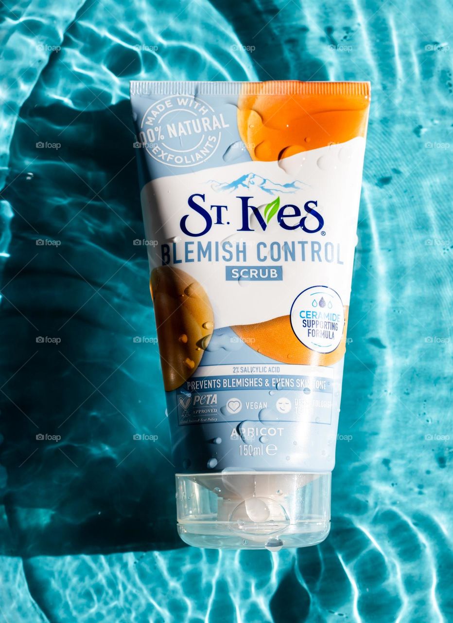 One tube of brand scrub. Ives with water droplets lies in the center on a blue background with shadows and highlights from the water, flat lay close-up. The concept of female cosmetics, body care, beauty.