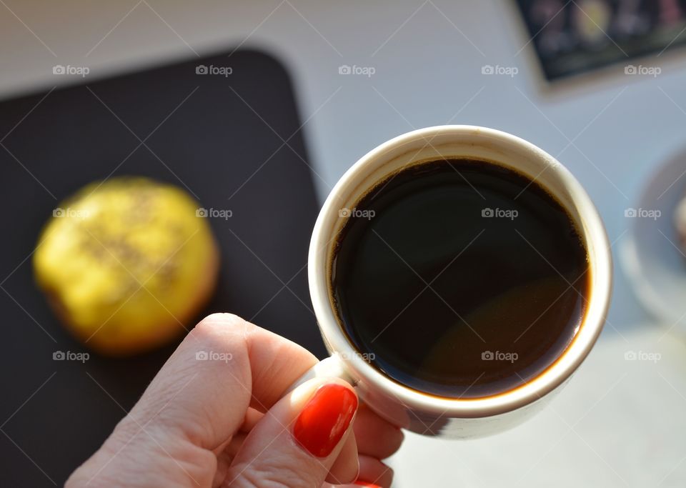 cup of coffee in female hand in sunlight on a white and brown background, top view, morning routine