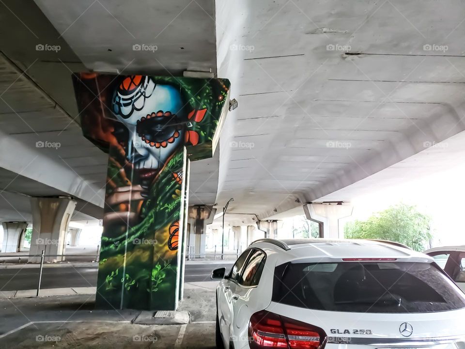 Visual street art on a cement highway pillar in a parking lot that celebrates Dia de los muertos/ Day of the dead. A Mexican cultural tradition of celebrating and remembering those that have passed. Artist: @PauLGaris0n13