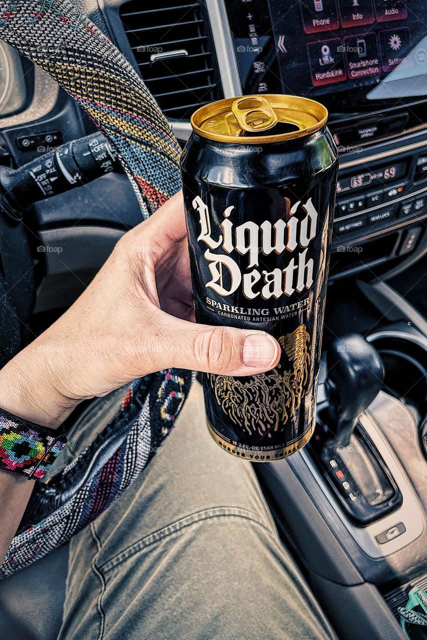 Drinking Liquid Death in the car, drinking water while driving, Liquid Death advertising, focusing on water in cans, saving the environment