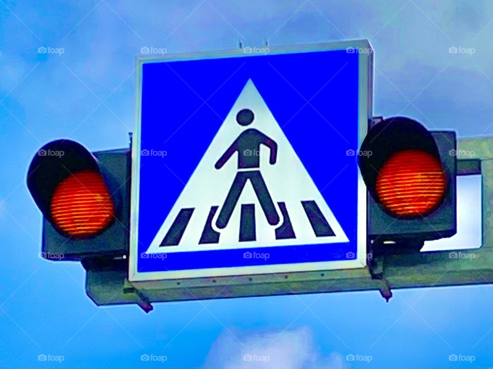 Flashing orange safety lights by a blue crosswalk sign.