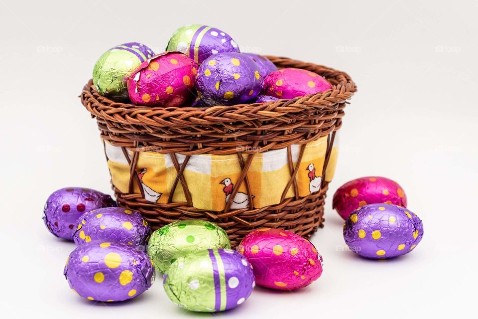 colorful foil covered Easter chocolate eggs, in a woven wooden brown basket, with a band of cloth covered with yellow chickens, around it