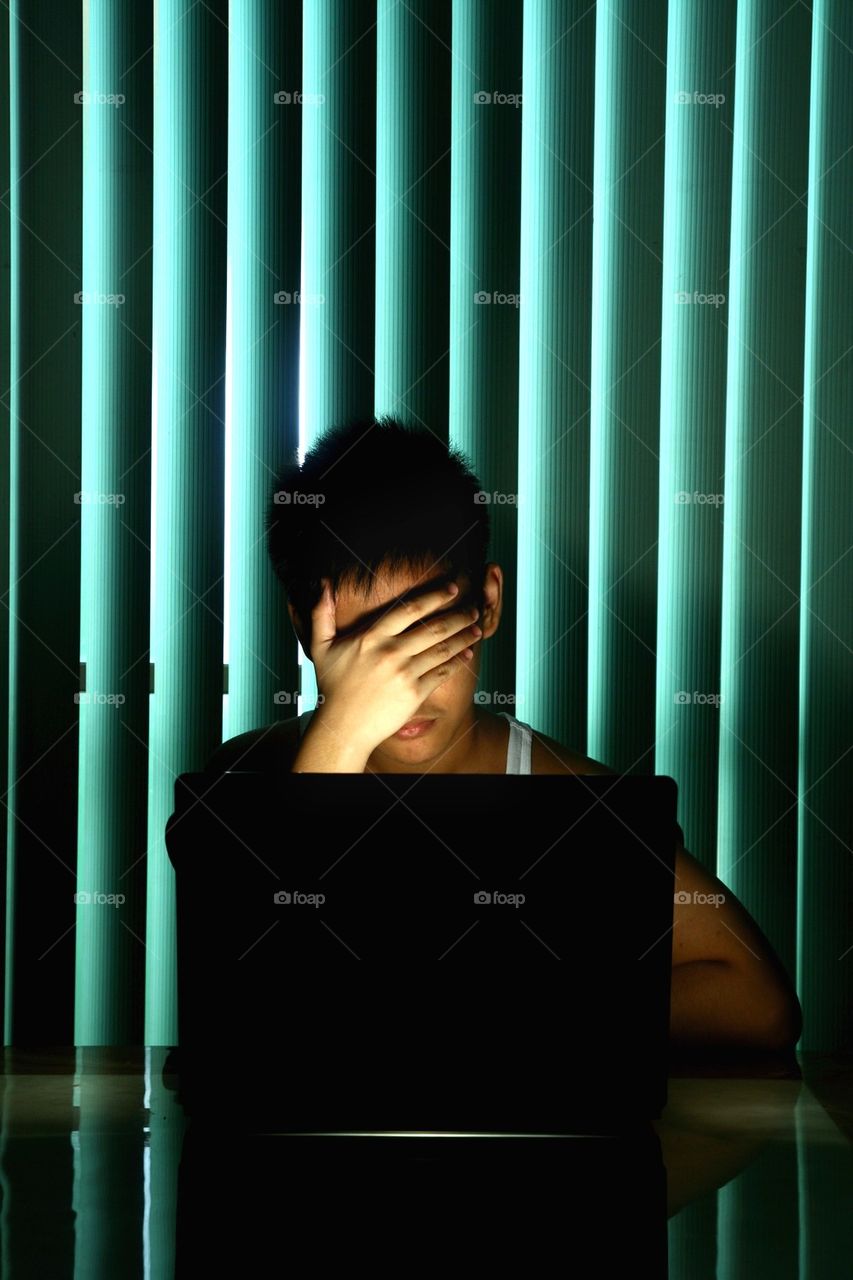 teenager in front of laptop computer covering his eyes