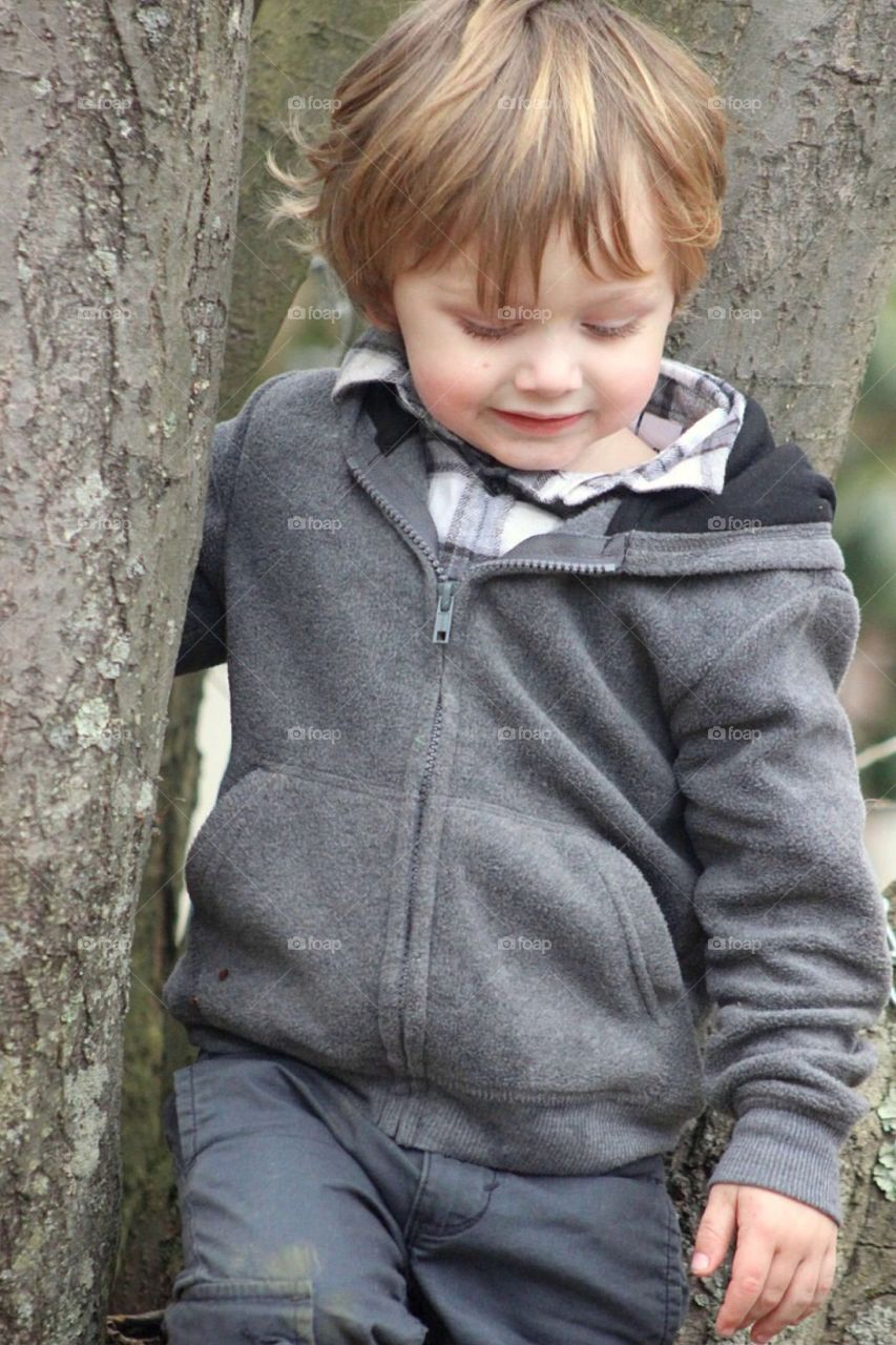 Little handsome boy standing near tree trunk