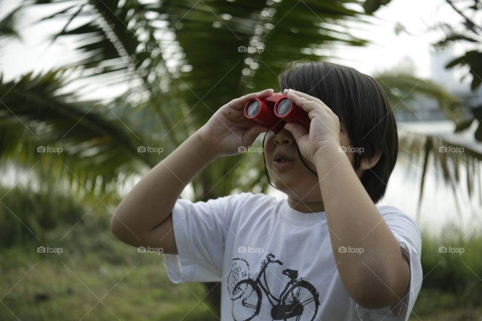 the adventurer, you boy looking through binoculars in the open outdoor with trees background out of focus
