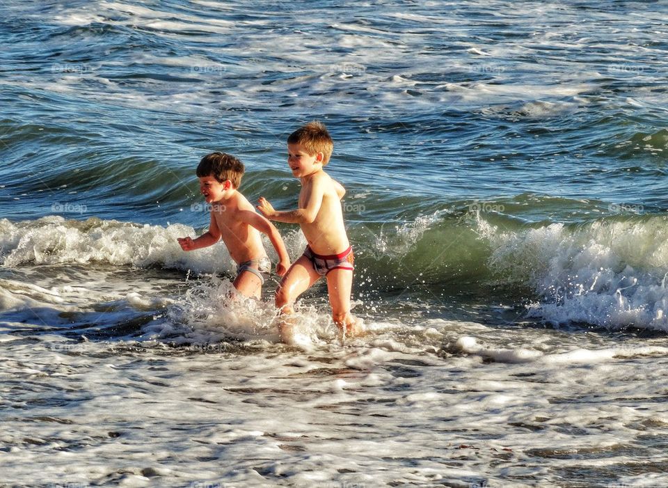 Two Young Brothers Splashing Joyfully In The Sea. Splashing In The Ocean