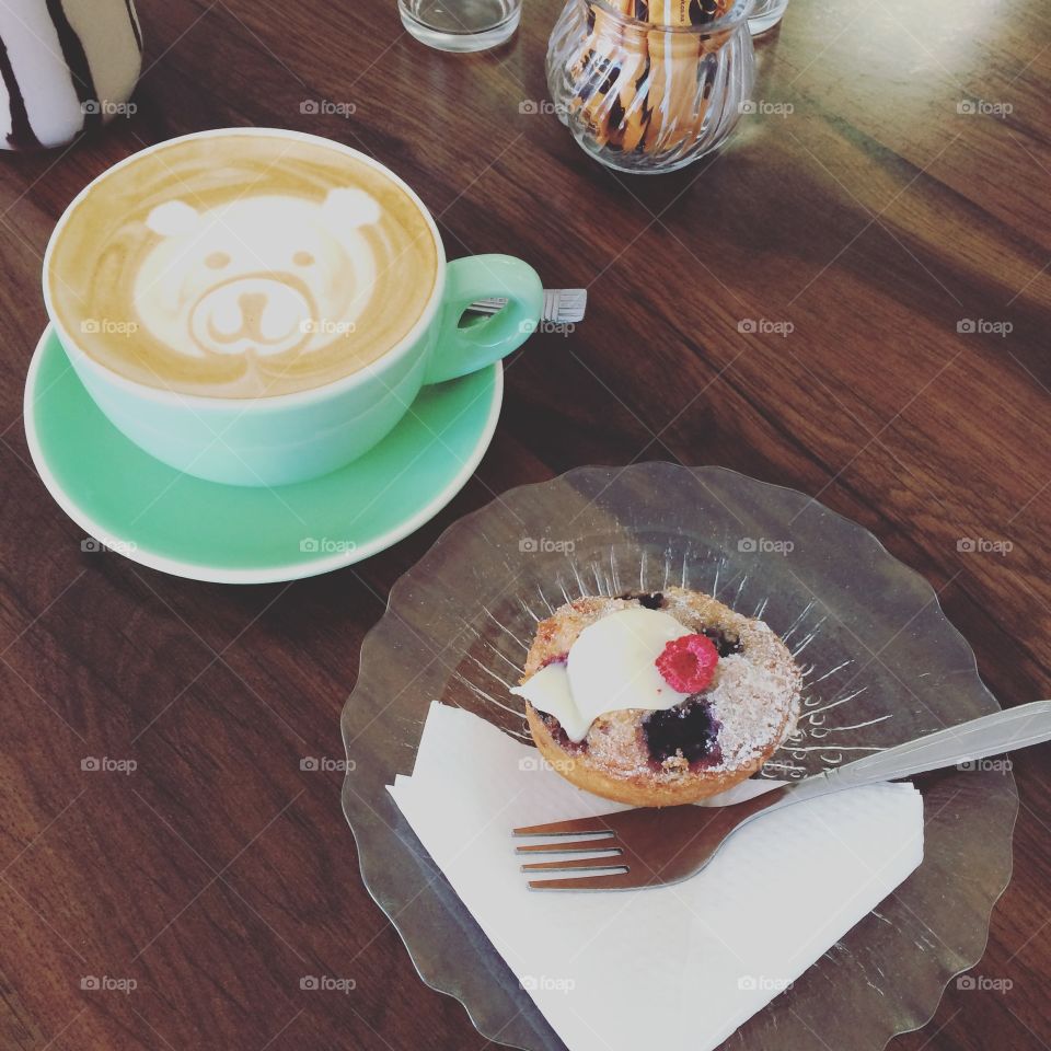 A gluten free blueberry, raspberry scone tests carefully in a glass dish beside a vanilla cappuccino in a quaint little coffee shop in Gibraltar. 