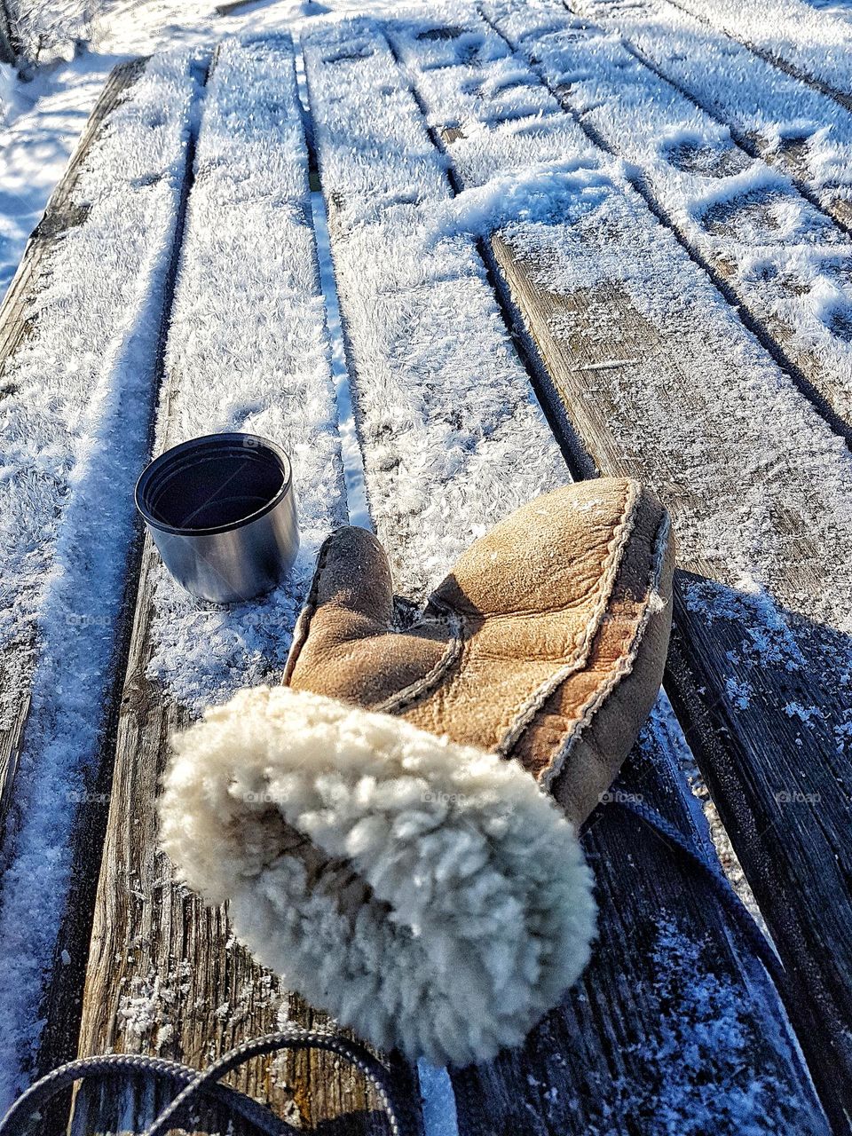 A brown fur glove and a cup on a wooden table covered in frost 