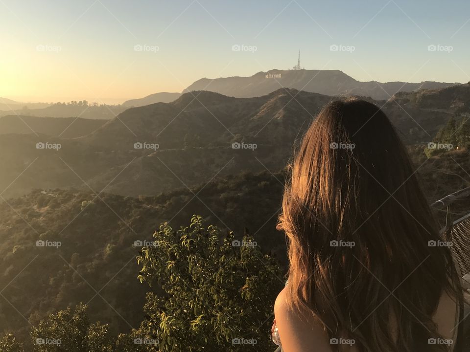 Brunette women looking out to the Hollywood hills as the sun starts to set with the hazy LA skyline beyond
