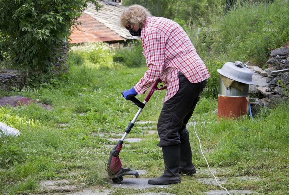 A woman cuts grass with a trimmer