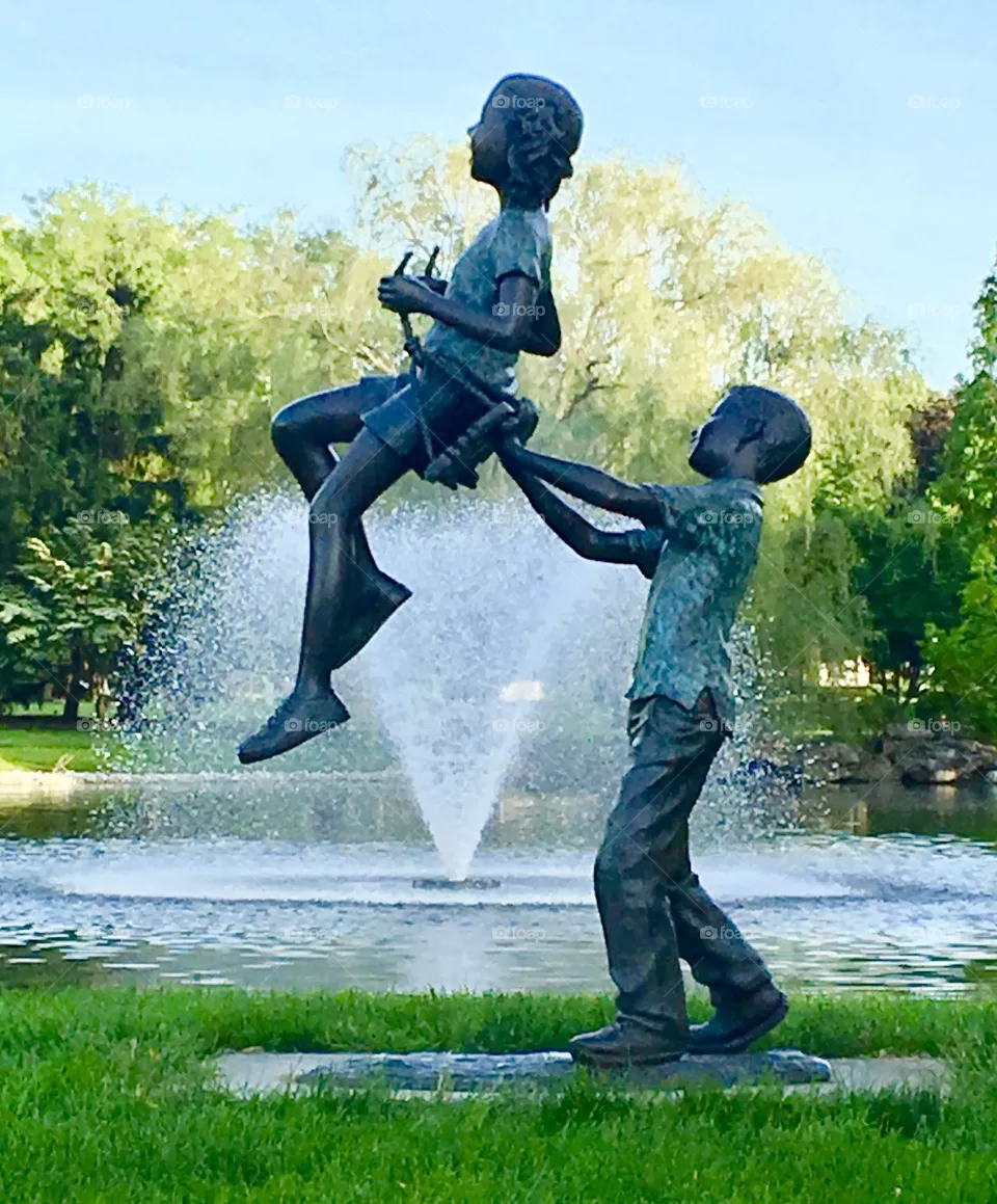 An amazing sculpture depicting the pure joy of childhood imagination. It shows a boy, pushing a girl on a swing while it appears that she’s being held up by only a spray of water from the fountain in the pond at our local park. 