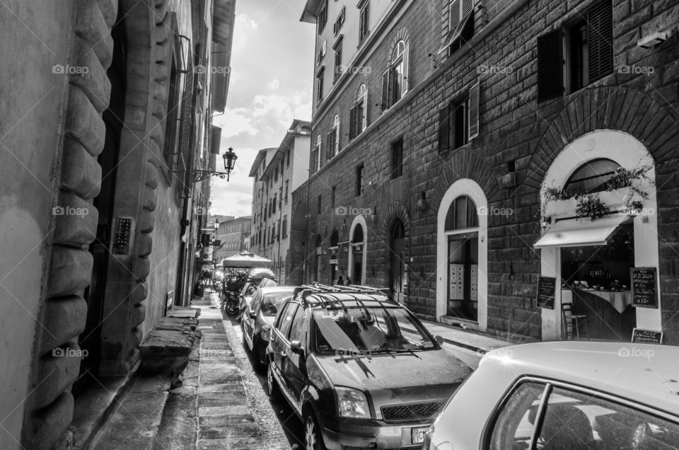 Cars parked and pedestrians in a street in Florence in black and white
