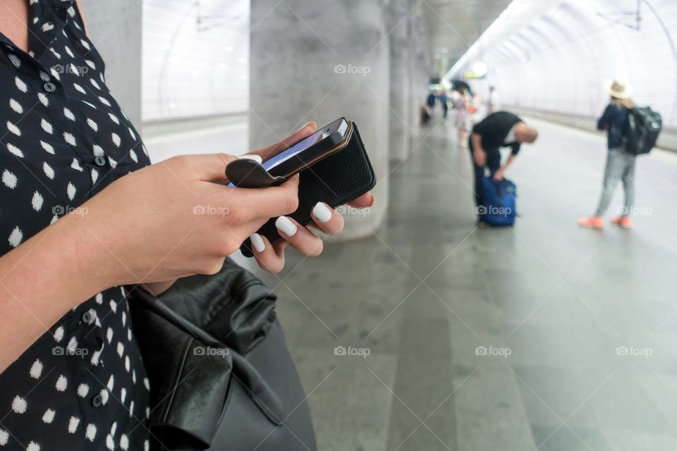 Woman with white long fingernails waiting for the train while using her cellphone