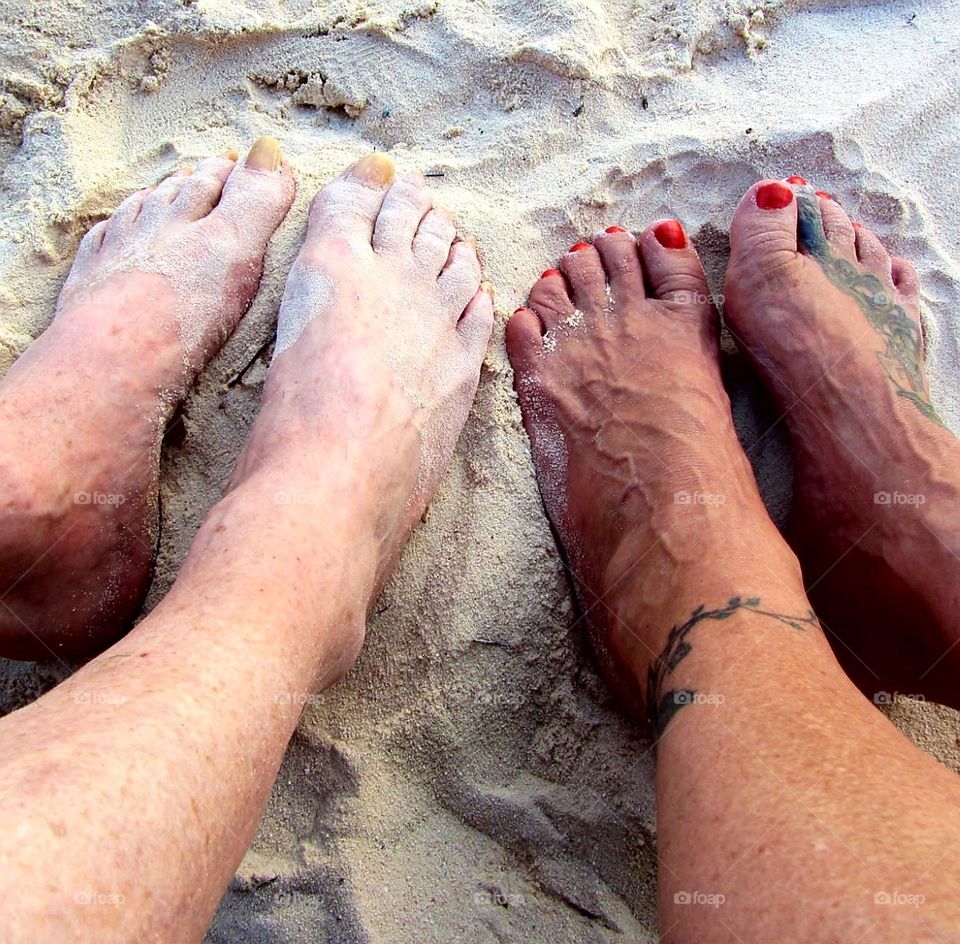 Two pairs of bare feet in tropical beach sand. I set is tanned, the other is not tanned at all. The girls nails are painted red. Happy feet on vacation.