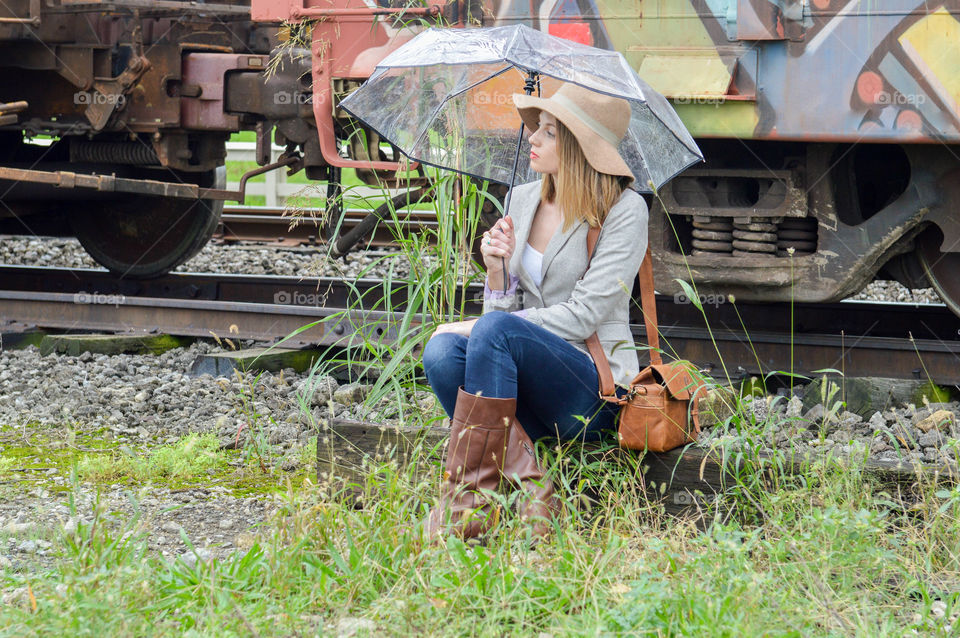 Woman sitting in front of a colorful train car with an umbrella