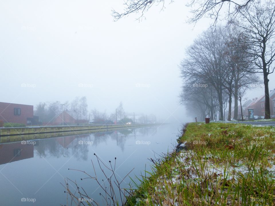 Winter day on the riverside with first snow in the grass under a grey misty sky