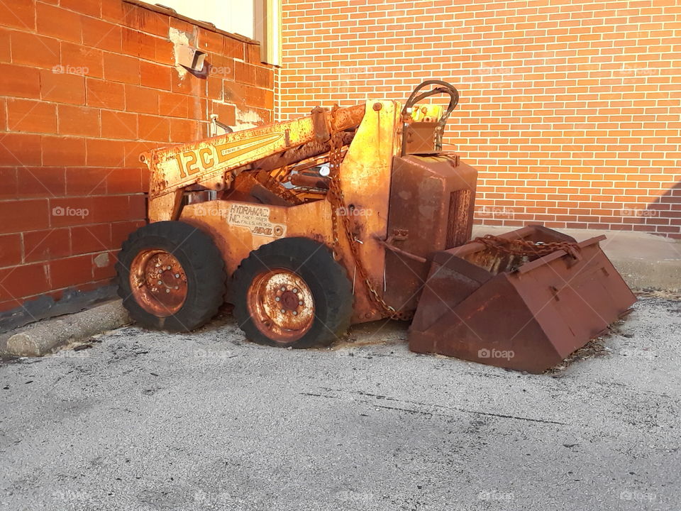 old tiny rusty bulldozer with a brick wall