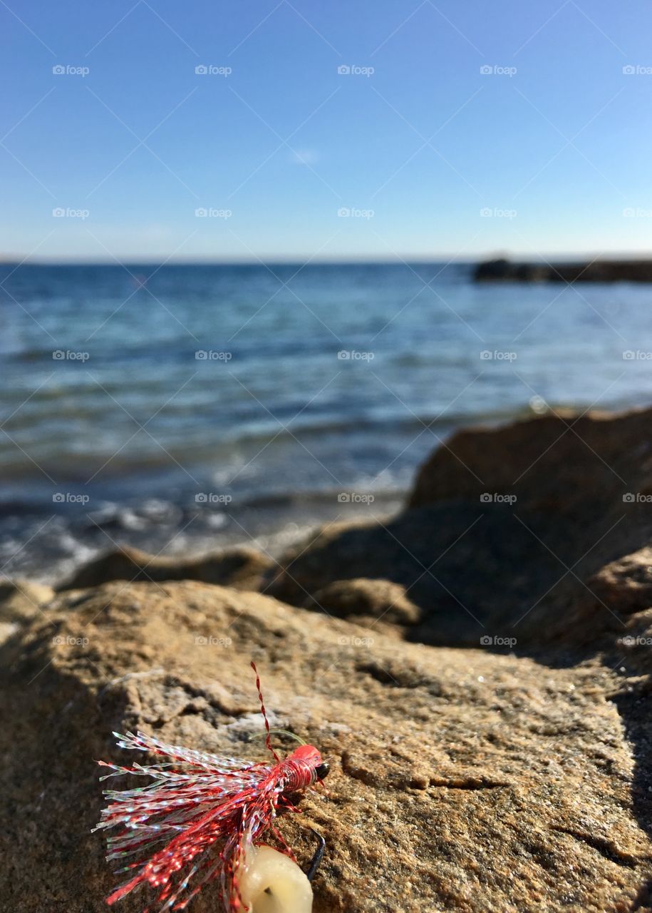 Red fishing lure on rock with ocean in background selective focus 