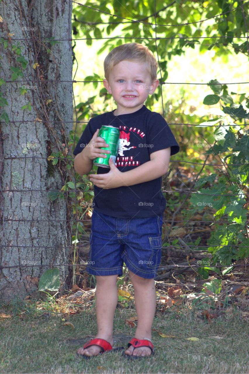 Little boy holding drink can near wire fence