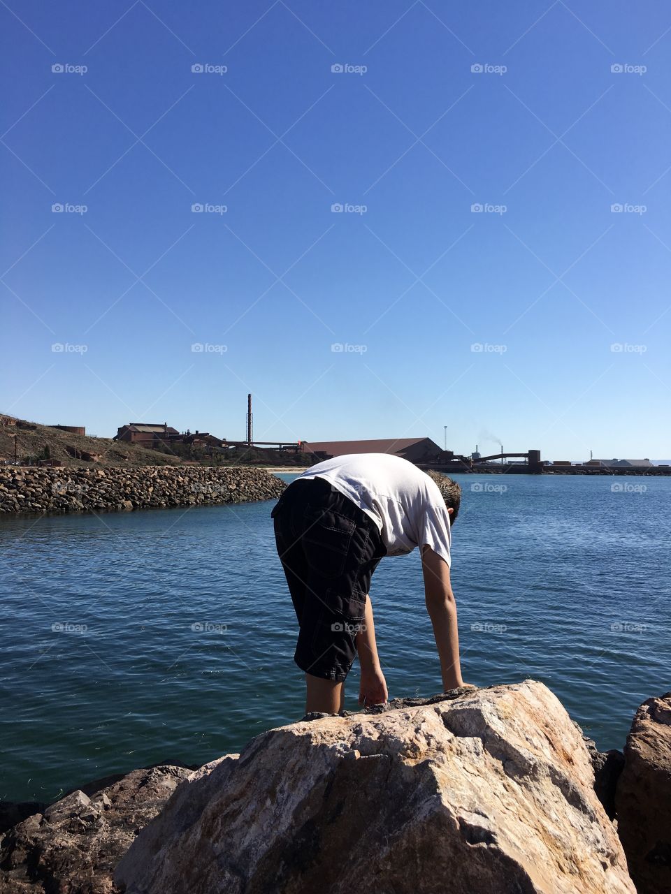 Boy on rocks by ocean in marina exploring summertime 