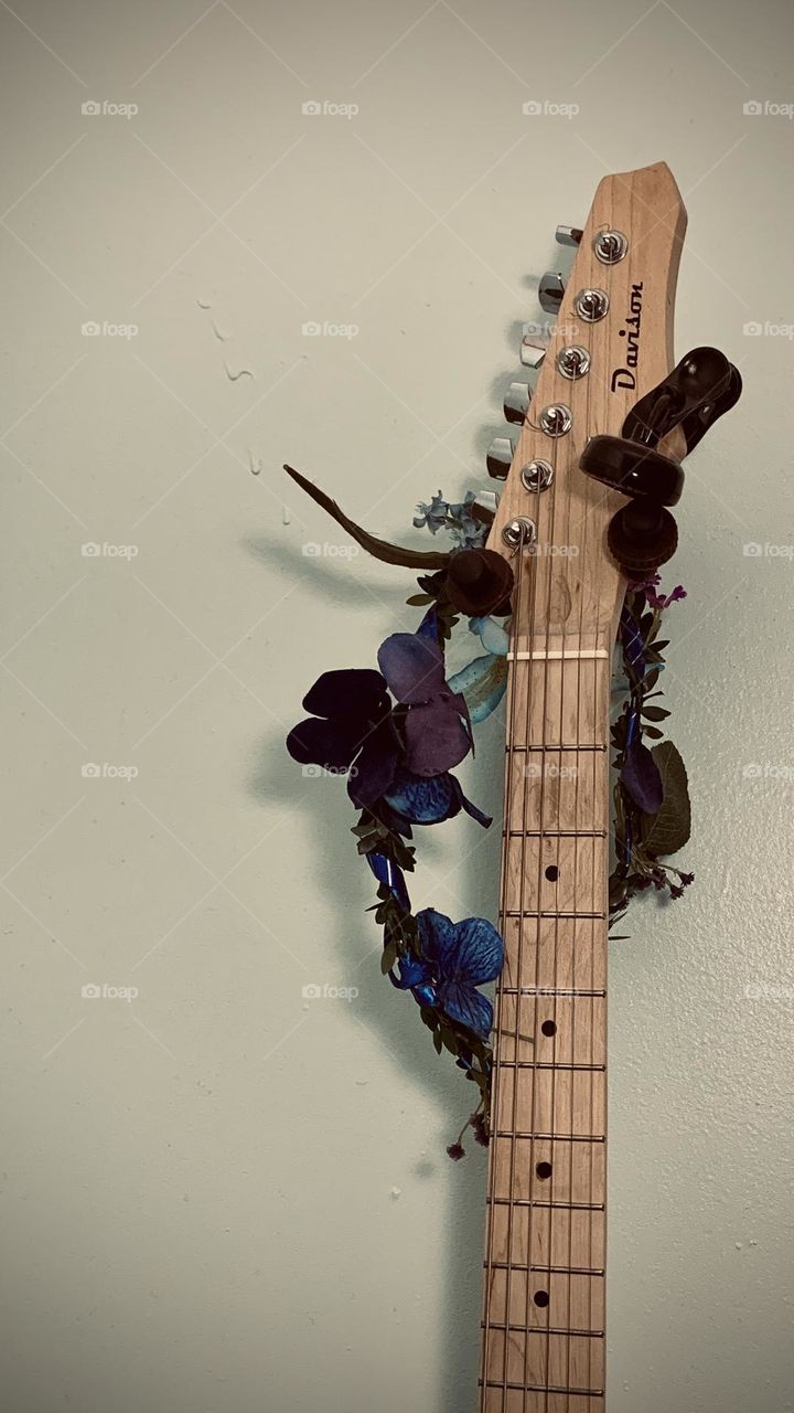 A Davison guitar hangs in a child’s bedroom, decorated with a blue and purple flower garland. 