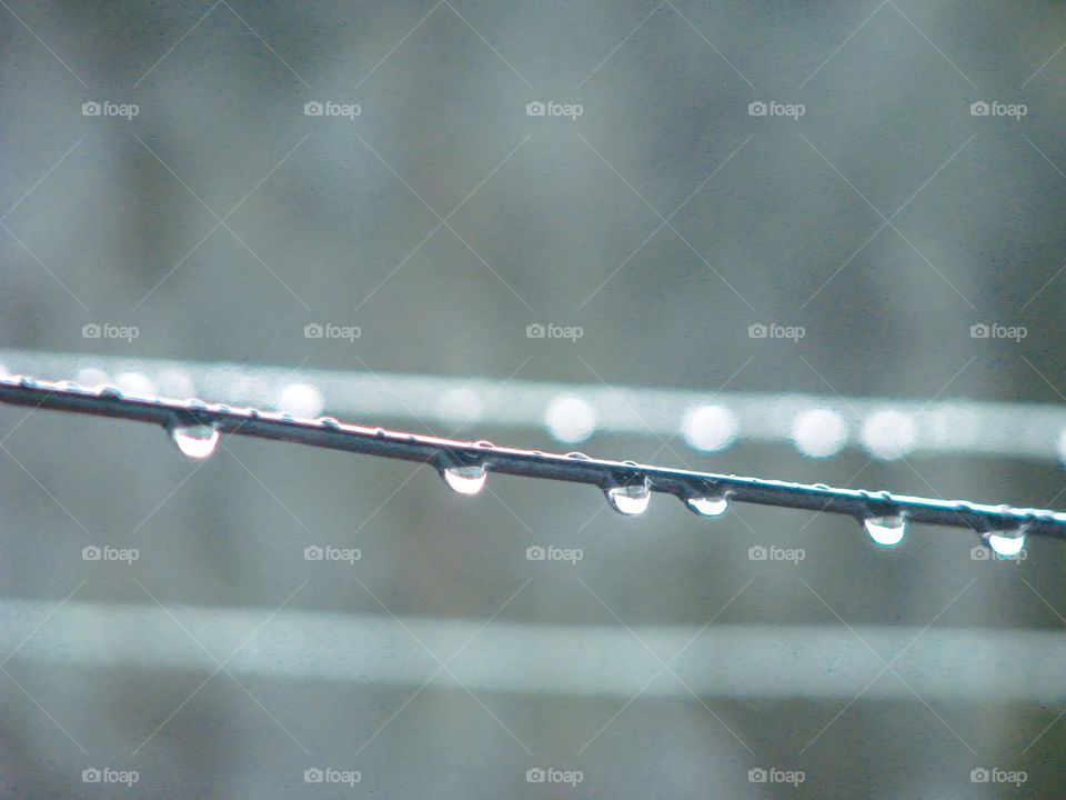 Close-up of a water drop hanging on a wire with a blurred background in low angle view