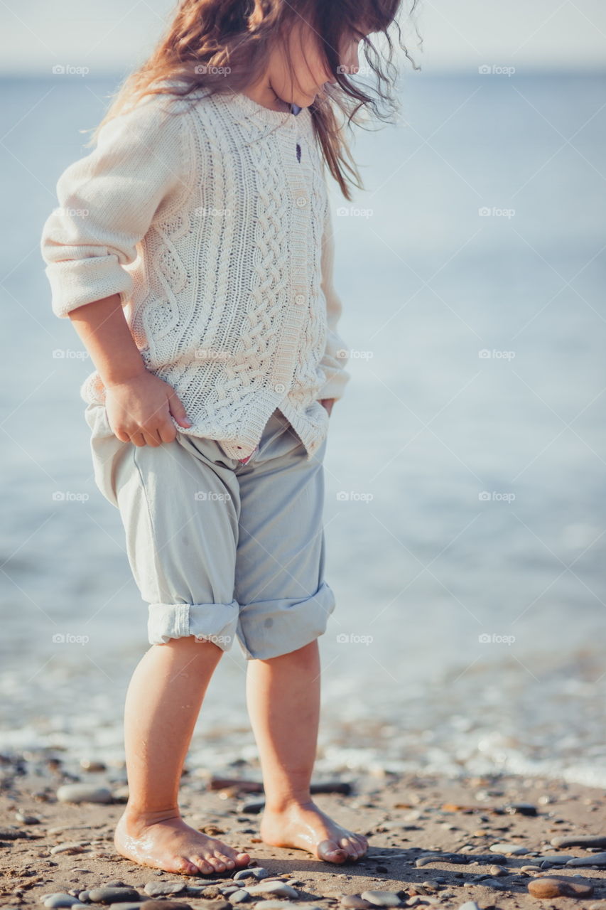 Little girl walking on the sea shore at sunny morning 