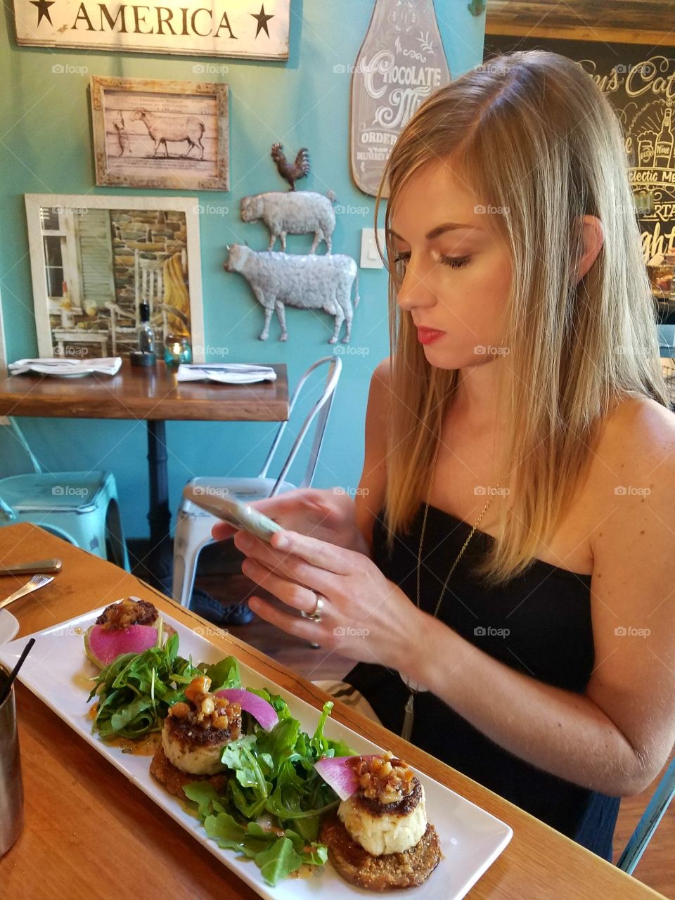 Woman on her cell phone at a rustic, farm inspired restaurant with a plate of food in front of her