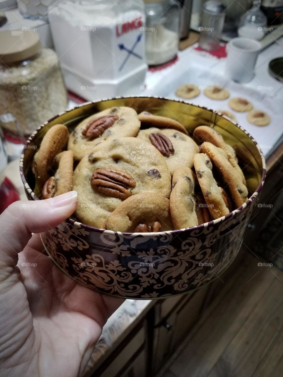 A woman holding a tin of Chocolate Chip Pecan Cookies in a kitchen