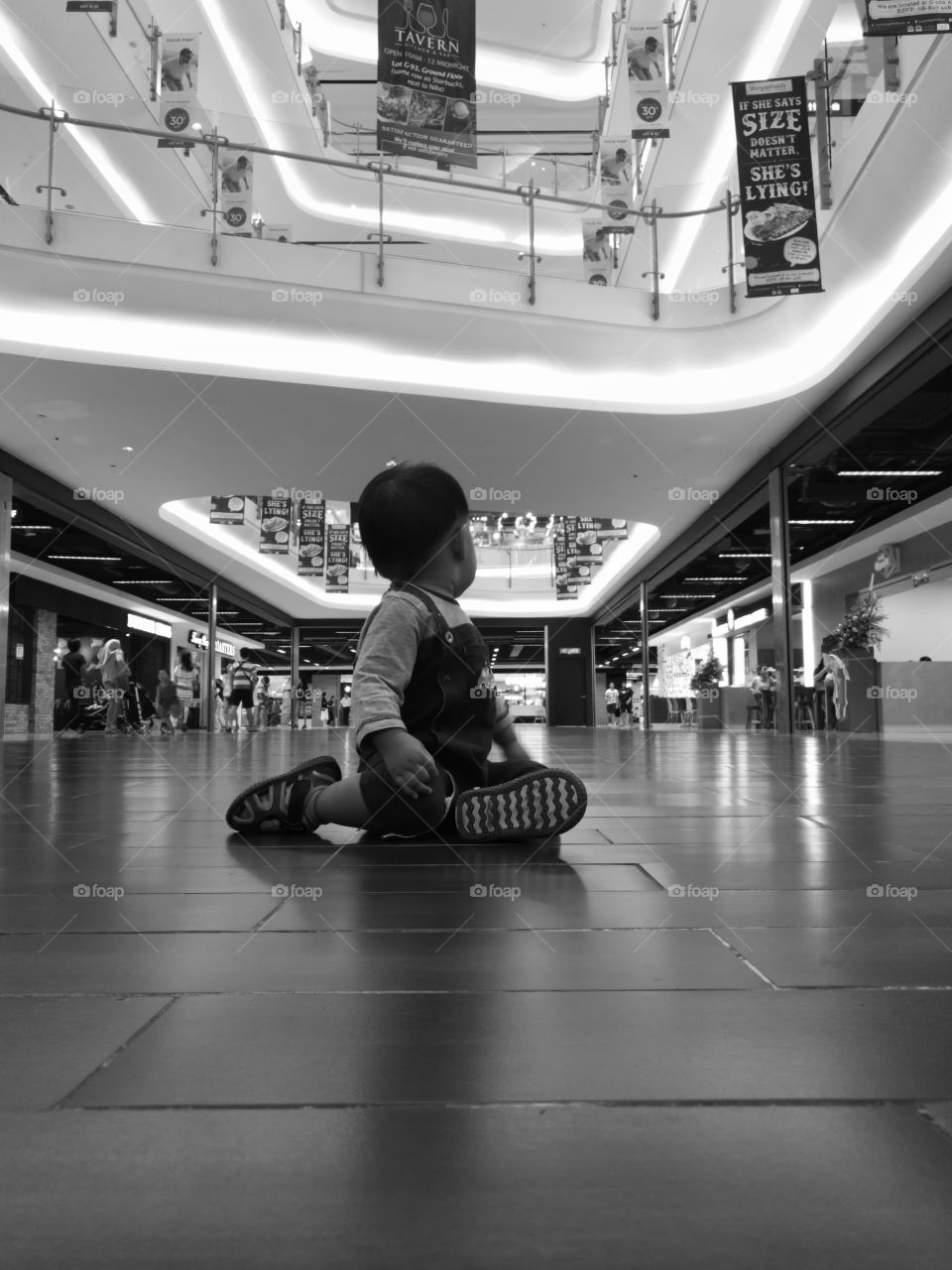My son sat on the floor of a shopping mall while turning his head to look behind him