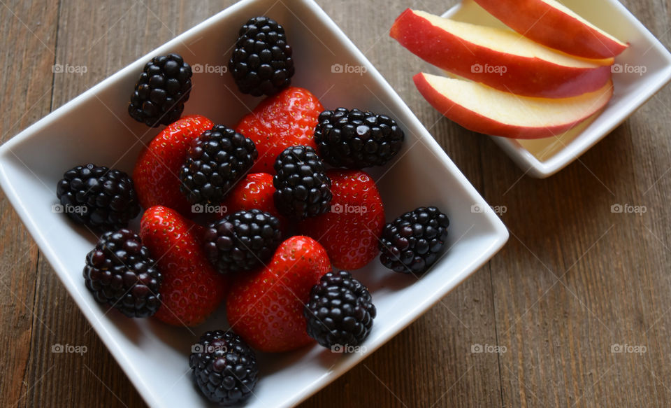 Bowl of strawberries and blackberries with apple slices on a wood background