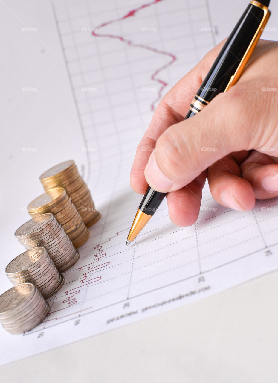 монеты ручка держит ручку на финансовом графике