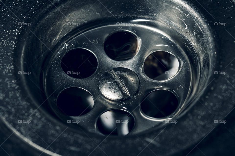 Dirty stainless steel sink drain close up with water drop. Soft focus, toned.