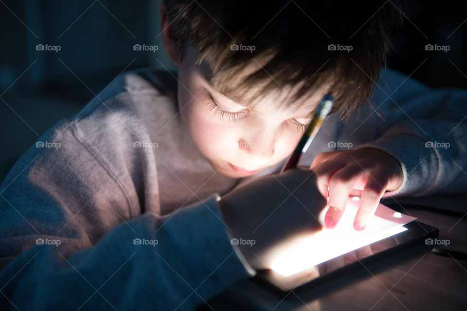 Candid, lifestyle close-up of a young boy's face illuminated by a brightly lit drawing tablet