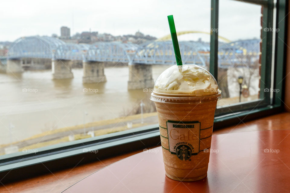 Starbucks frappachino cup on a table at a Barnes and Noble cafe with a view of a river, bridge and city in the background