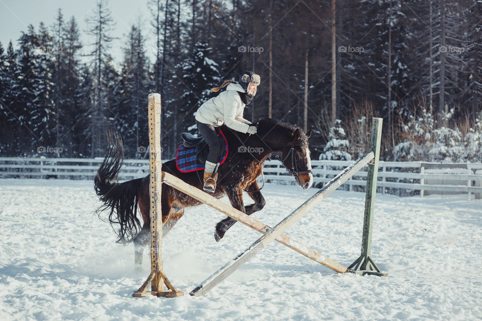 Teenage girl horseback jumping at cold winter day