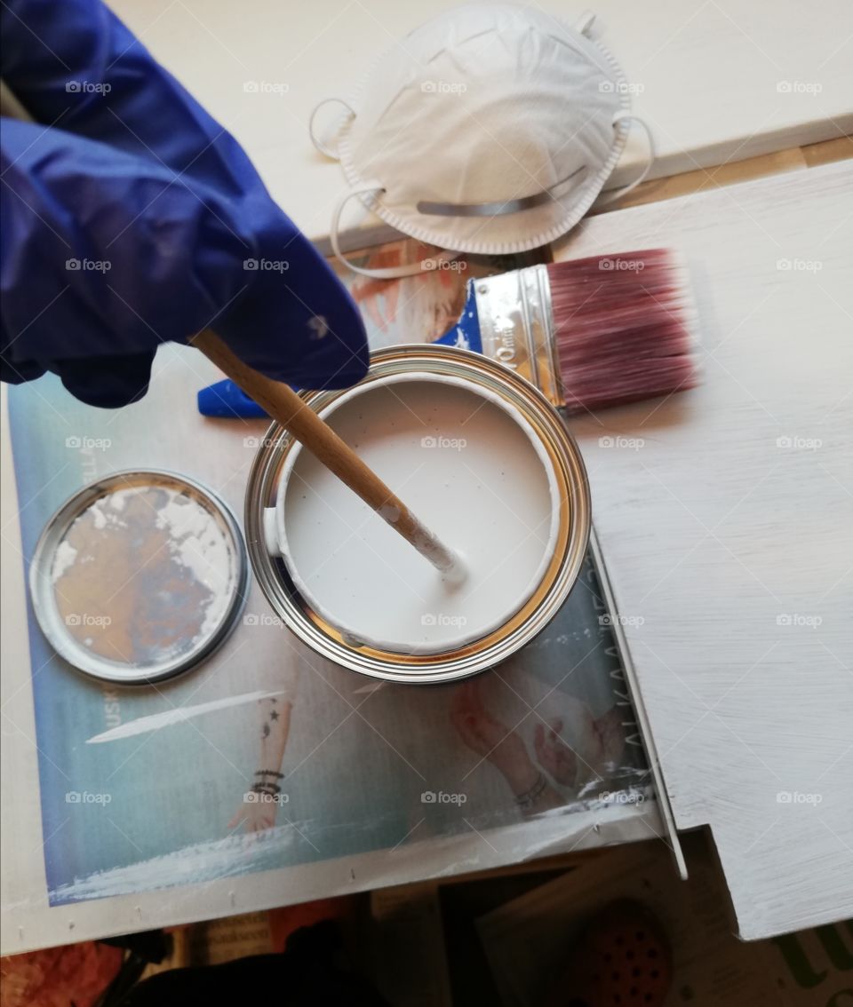 A respirator mask, a paintbrush, blue gloves and a stick in a water-soluble paint on a board and a newspaper.