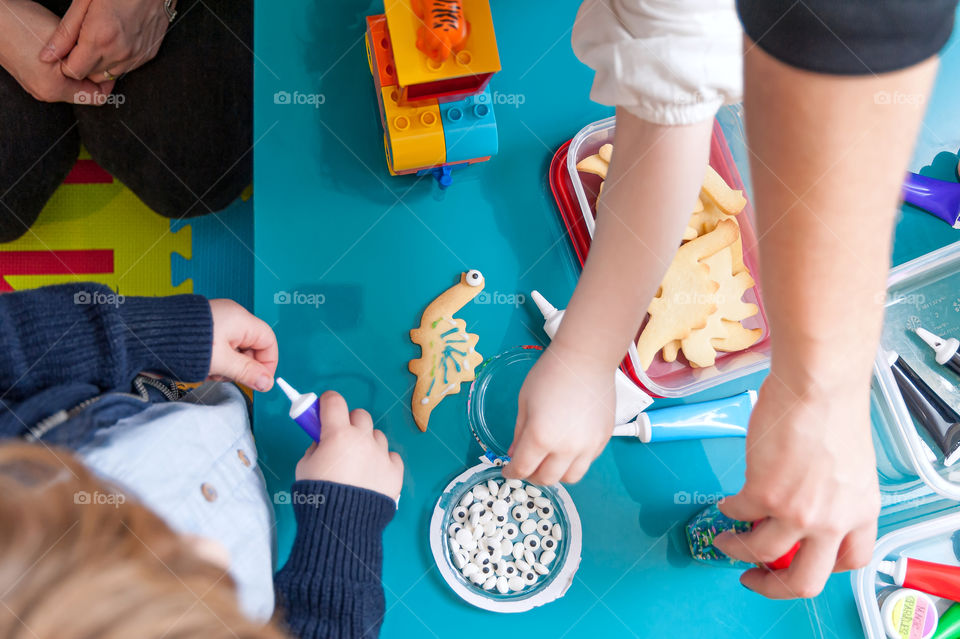 Children having fun decorating dinosaur shaped cookies.