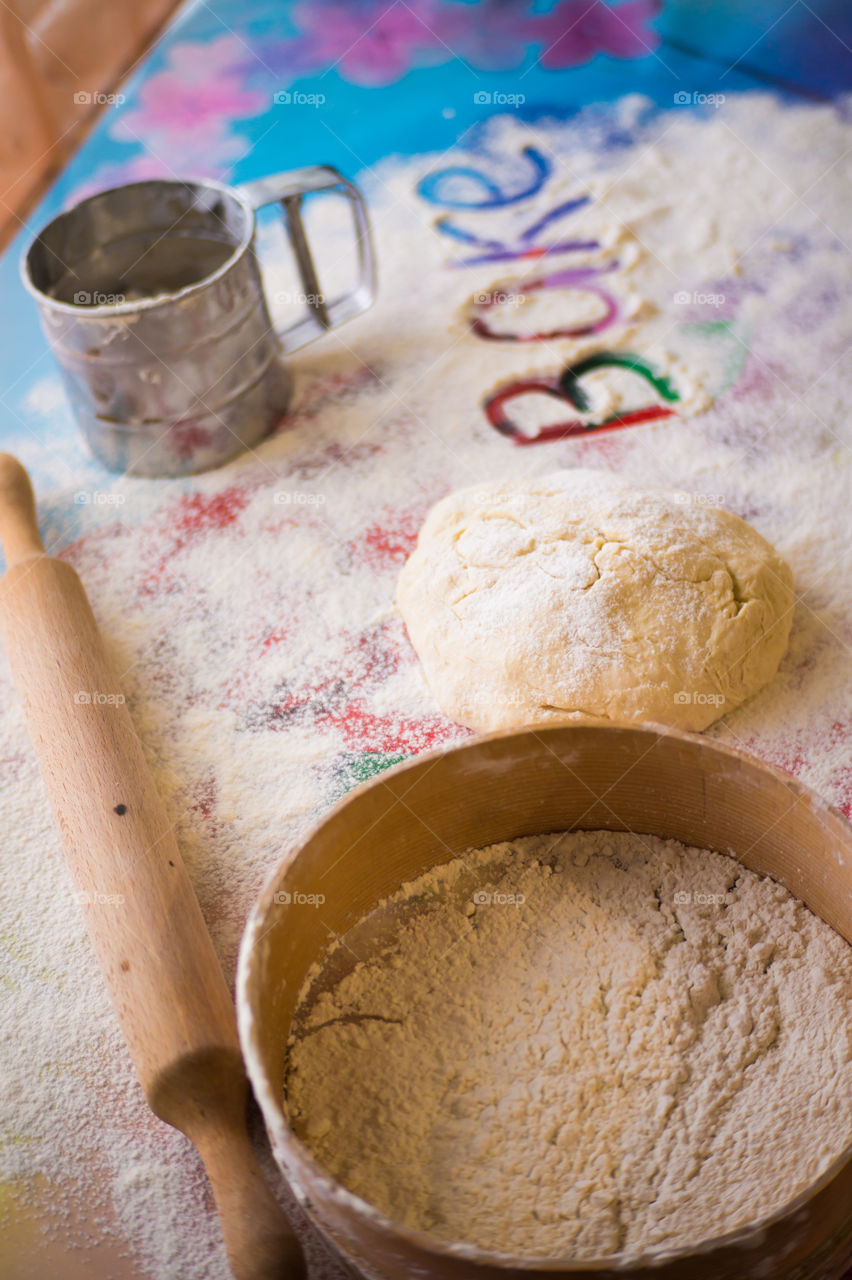 On the table lies a pastry for pies with sprinkled flour and a seeder for flour. Written to bake on the table.