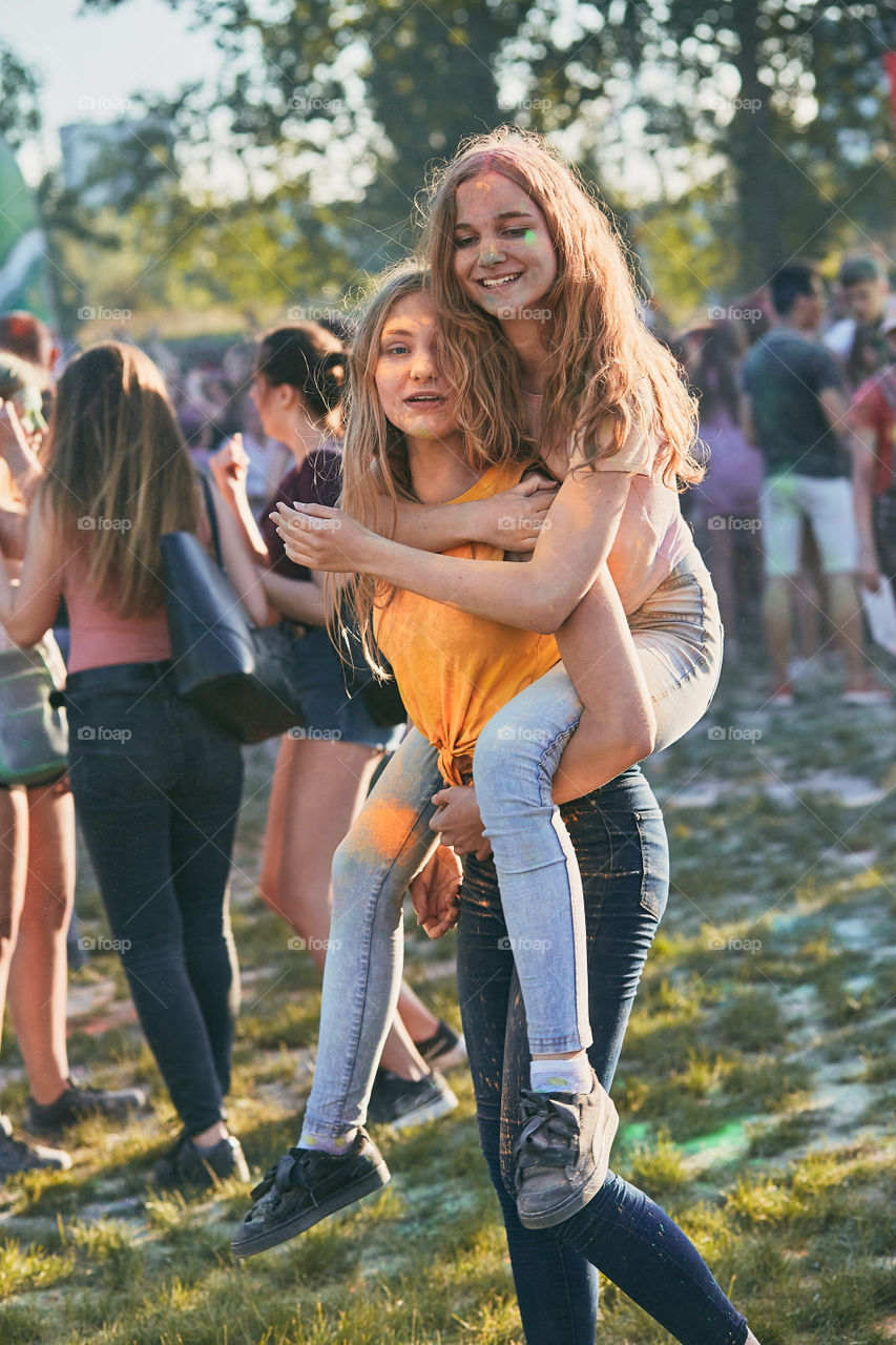 Portrait of happy smiling young girls with colorful paints on faces and clothes. Two friends spending time on holi color festival. Real people, authentic situations