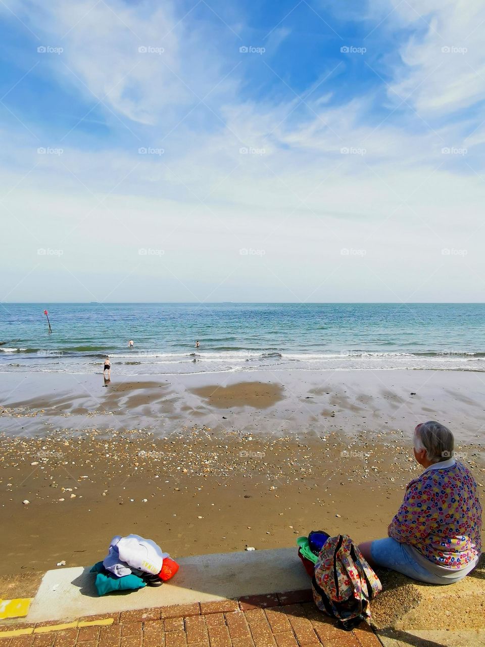 Grandmother looks at the seashore and waits for her grandchildren who are swimming. April. Sunny spring weather. Beginning of the swimming season in England. Isle of Wight.